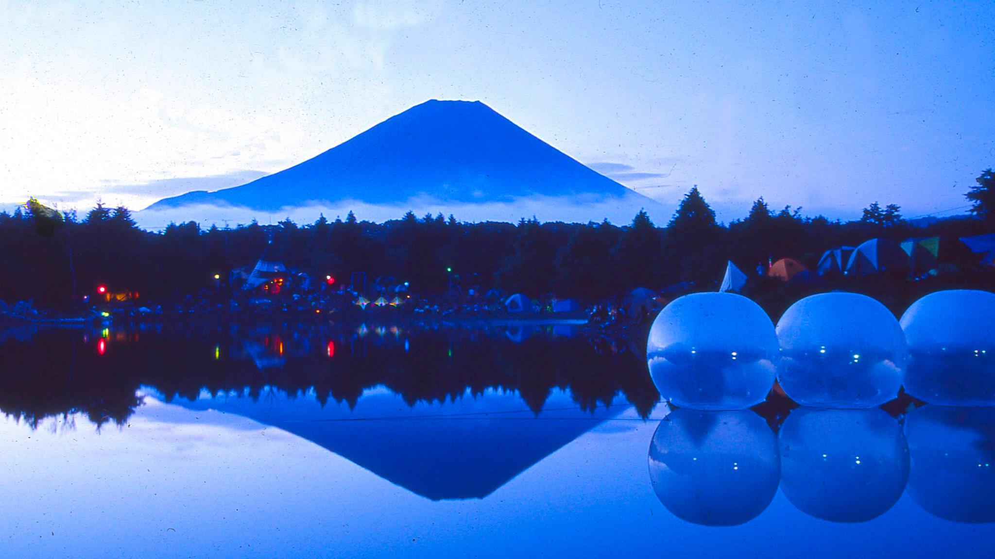 “SOLSTICE MUSIC FESTIVAL” (2001) at Motosu Highland, Yamanashi Prefecture
“SOLSTICE MUSIC MUSIC” was held at Motosu Highland in 2001. The person I want you to pay attention to is Masaru Morita, who led a VJ team called M.M. Delight. He passed away in 2008, but he was one of the leading figures of outdoor parties in Japan and later established the Nagisa Music Festival and other notable events. Morita-san projected the moving images on round balls floating on the lake” (Kotaro)
Photography Kotaro Manabe