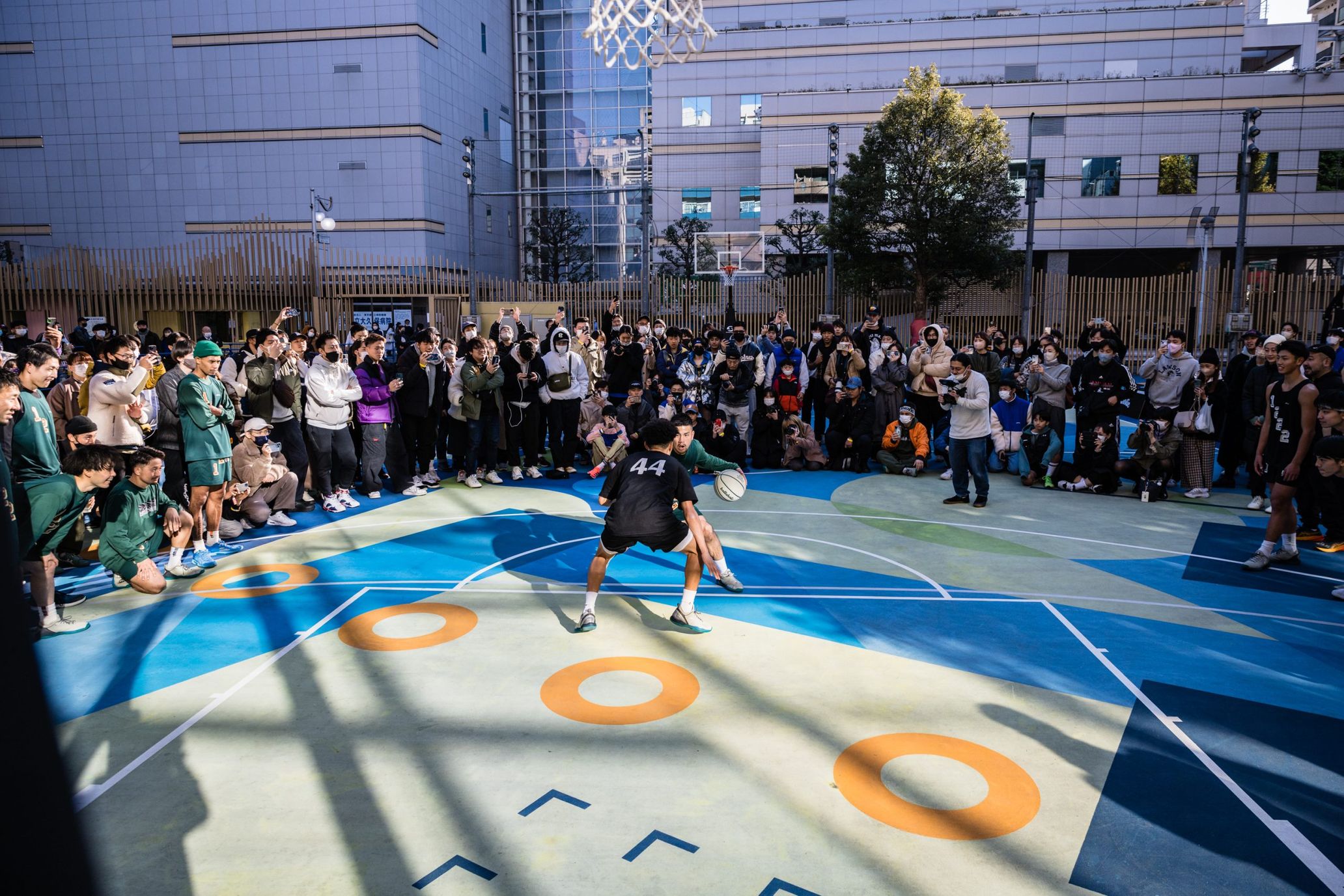 東京都新宿区にある大久保公園のアートコートでの写真集お披露目ピックアップイベントのひとコマ。ここは、アメリカ2K財団とNBAスーパースターのケビン・デュラントのチャリティ基金（KDCF）の両者によるコミュニティ支援プログラムの初のアジアプロジェクトとして、アートコートへと改修された場所。それを手掛けたのはアーティストのFATEと一般社団法人「go parkey」。代表のABとは、TANAはストリートボールを通じて、数多くのボール・オン・ジャーニーをともにしてきた